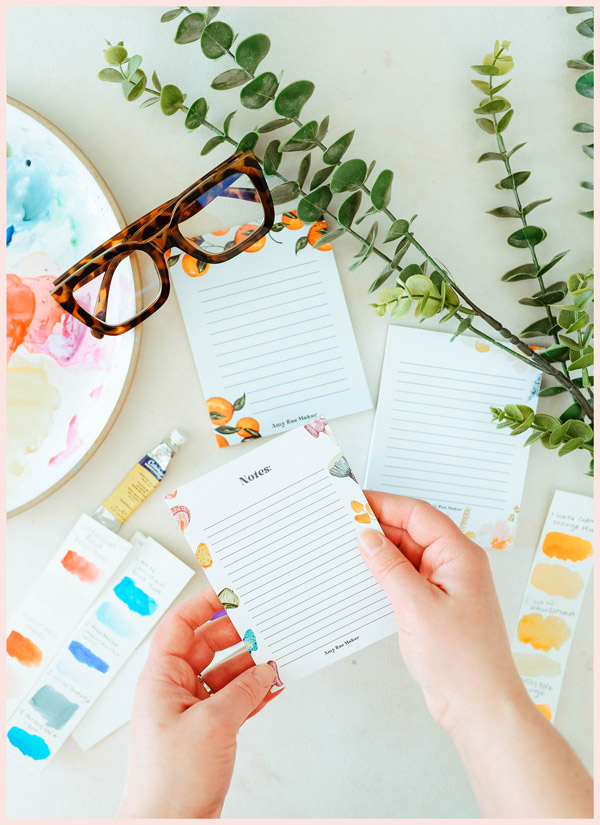 A topdown view photo of glasses, some plants and some notepads on a table.
